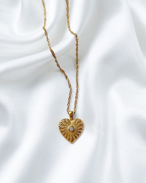Aukso spalvos kaklo papuošalassu širdelės medalionu.